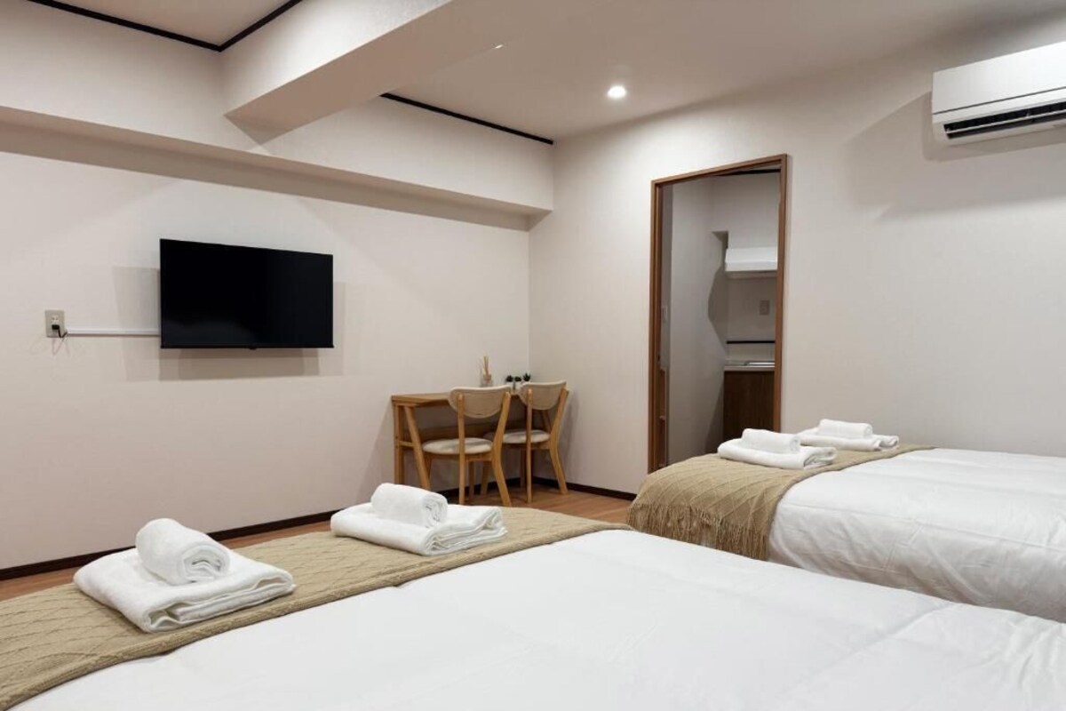 Una camera d'albergo con due letti, una TV a schermo piatto, una sedia di legno e uno specchio.