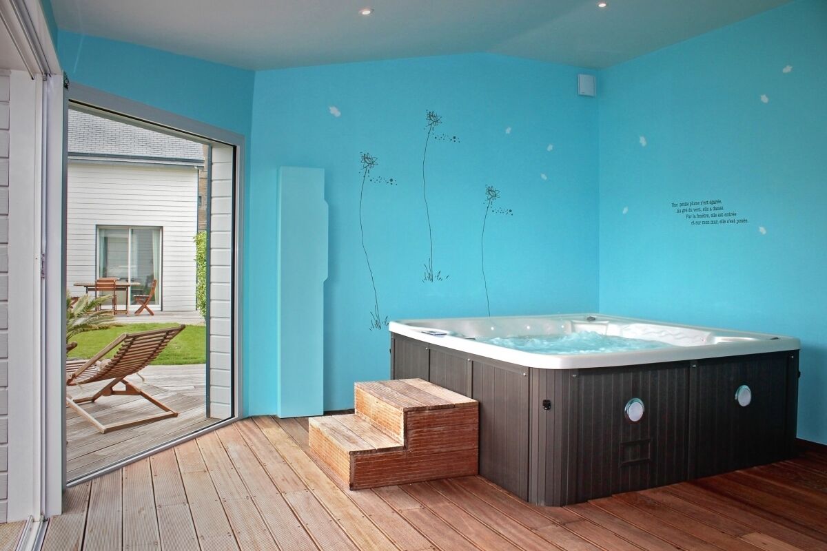 A modern bathroom with a hot tub, wooden steps, and a view of a patio with outdoor furniture.