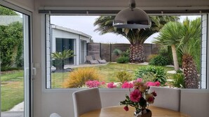 Zona pranzo con tavolo e sedie, un vaso con fiori e vista su una casa e giardino moderni attraverso ampie finestre.