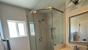 Ein modernes Badezimmer mit einer Duschkabine, einer Toilette, einem Waschbecken mit Spiegel und einem Fenster.