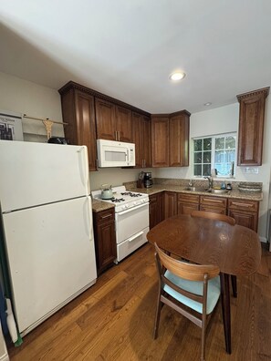 A kitchen with wooden cabinets, a white refrigerator, a stove, a microwave, and a dining table with chairs. - Spacious, Comfy and Charming Studio in Granada Hills, LA (Los Angeles)