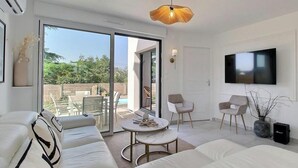 Una sala de estar moderna con un sofá, una mesa de centro y un televisor. Hay una puerta corredera de vidrio que da a un espacio exterior con piscina.