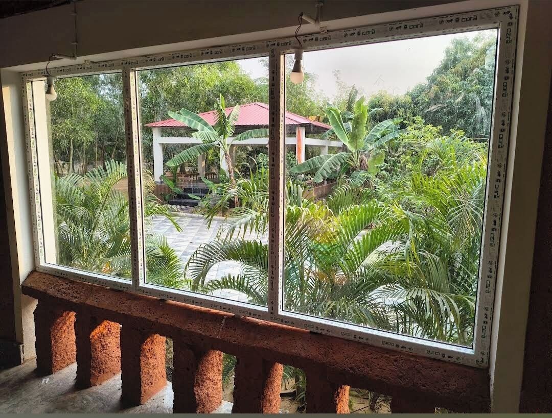 Una ventana con vista a un jardín, una estructura de techo rojo y un banco de piedra.