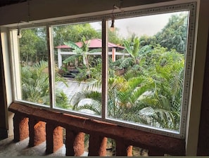 A window with a view of a garden, a red-roofed structure, and a stone bench.