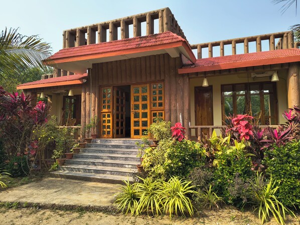 A wooden house with a red-tiled roof, wooden porch, and a staircase leading to the entrance.