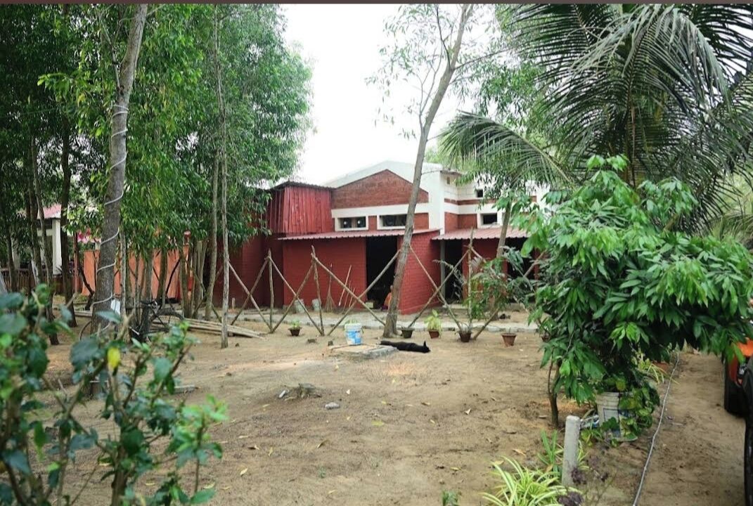 Un edificio con fachada roja y blanca, rodeado de árboles y plantas en macetas.