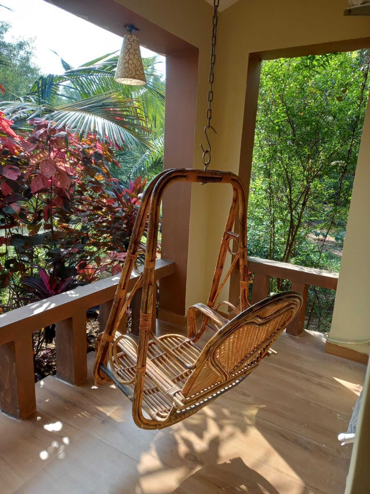 A wicker swing chair on a wooden deck with a view of lush greenery.