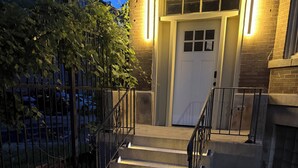 En byggnads entré med en trappa av betong, ett metallräcke och en dörr med ett fönster.