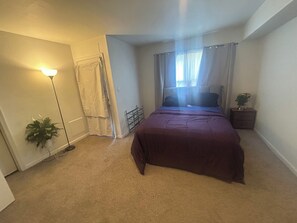 A bedroom with a bed, a nightstand, a floor lamp, a window with curtains, and a potted plant. - Cozy 1-bedroom condo in Hampton/AC  NASA ,Air Force ,Army base Hampton U Norfolk (Hampton)