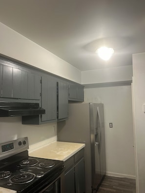 A compact kitchen with a stove, cabinets, and a refrigerator.