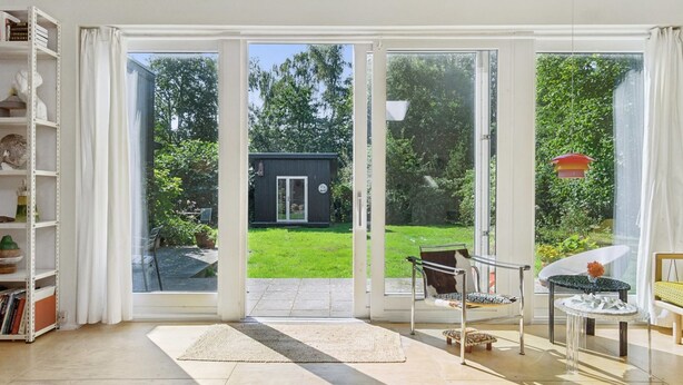 A room with a large sliding glass door leading to a garden, a bookshelf, and a small table with a vase. - "Verna" - 450m from the sea by Interhome (Ebeltoft)