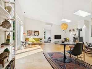 Ein modernes Wohnzimmer mit einem gelben Sofa, einem Esstisch mit Stühlen, einem Kamin und einem Bücherregal mit Dekoration.