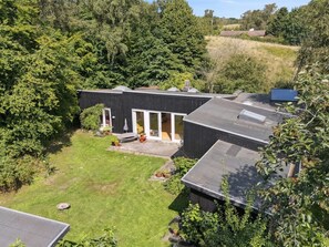 Ein modernes Haus mit großem Garten, einer Terrasse mit Gartenmöbeln und einer Garage.