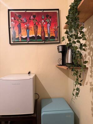 Una cocina con un refrigerador blanco, un mini refrigerador azul, una cafetera sobre una repisa y una planta en maceta.