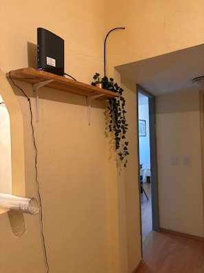 A room with a wooden shelf holding a black device and a hanging plant. - Del Sol Suite: Ideal for travelers who enjoy a quiet place to relax (Puerto Vallarta)