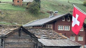 A rustic building with a stone foundation, a wooden structure on top, and a red flag with a white cross. - Haus Petunia by Interhome (Saas-Grund)