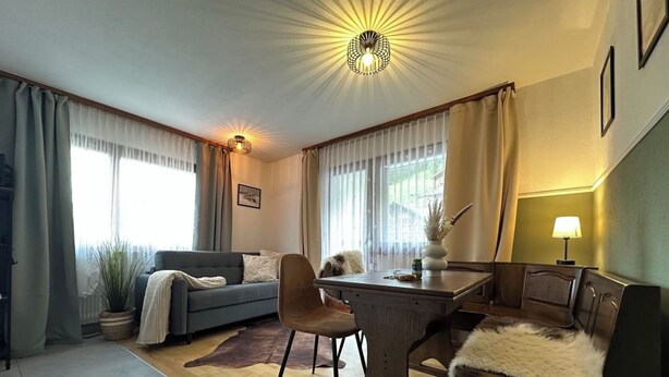 A modern living room with a sofa, a dining table, and a lamp. - Haus Petunia by Interhome (Saas-Grund)