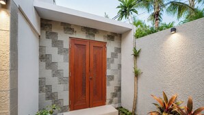 Un edificio moderno con una puerta doble de madera, un muro de piedra y un pequeño jardín con plantas.