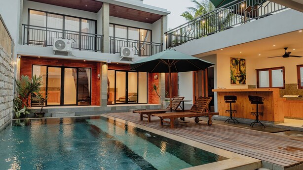 Una casa moderna de dos pisos con piscina, mobiliario exterior y un balcón.
