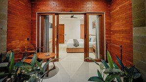 Una habitación con pared de ladrillo, cama, ventilador de techo y vista a otra habitación.