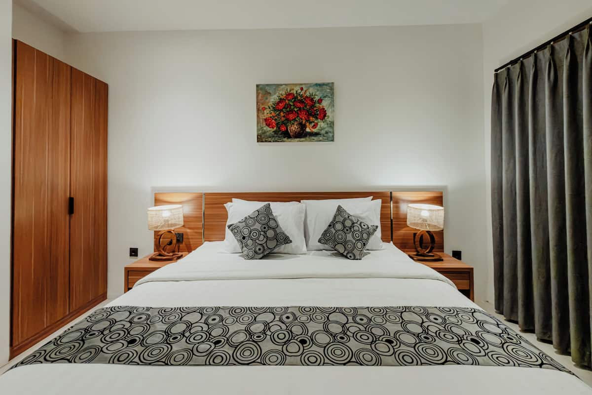 Un dormitorio con cabecera de madera, dos lámparas de noche, una colcha estampada, un cuadro de flores en la pared y un armario.