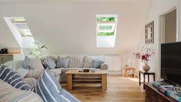 A living room with a sofa, a coffee table, a TV, and a window with a view of greenery.