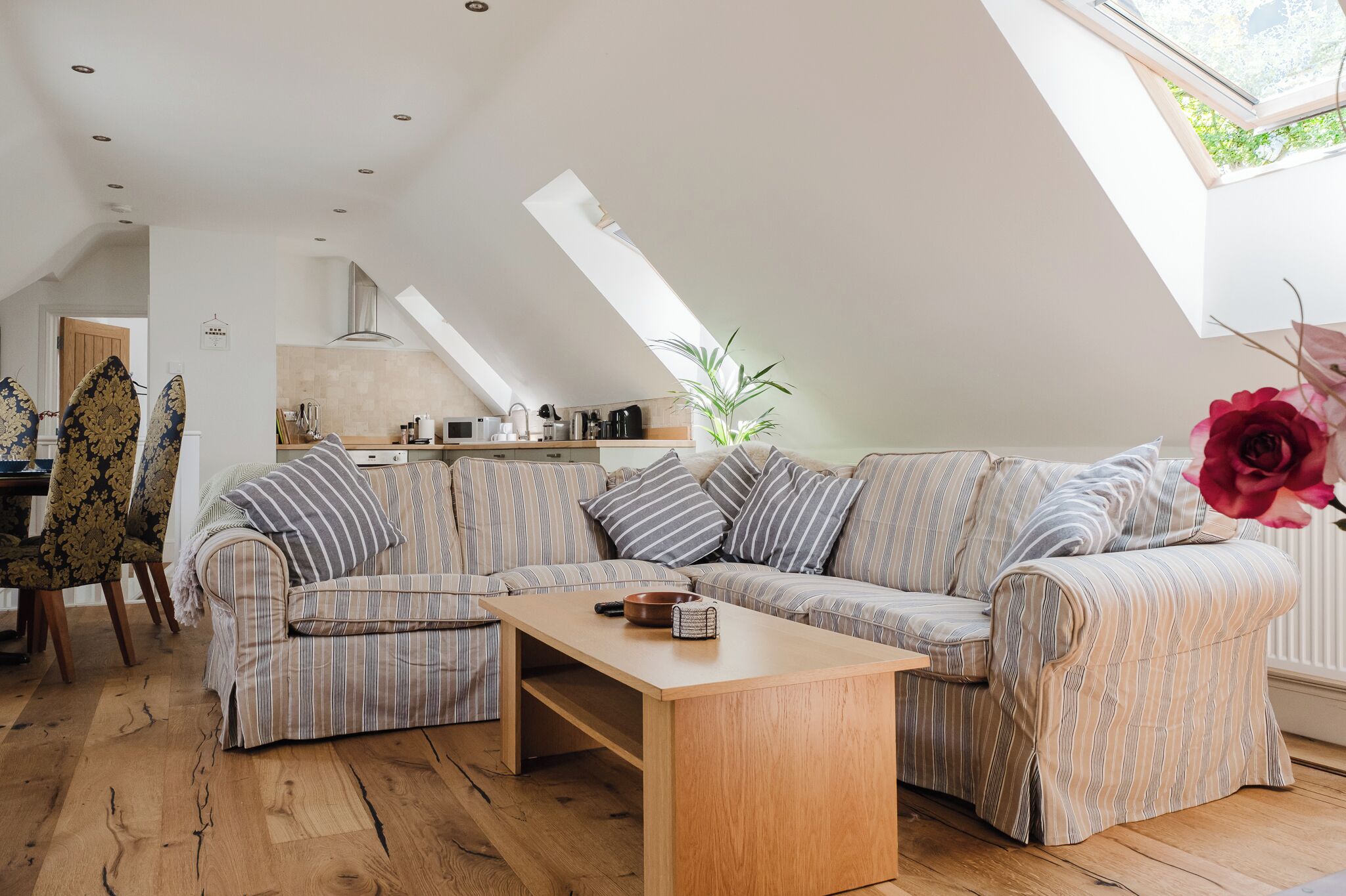 A loft-style living room with a wooden coffee table, striped sofa, and a dining area with a chair and table.