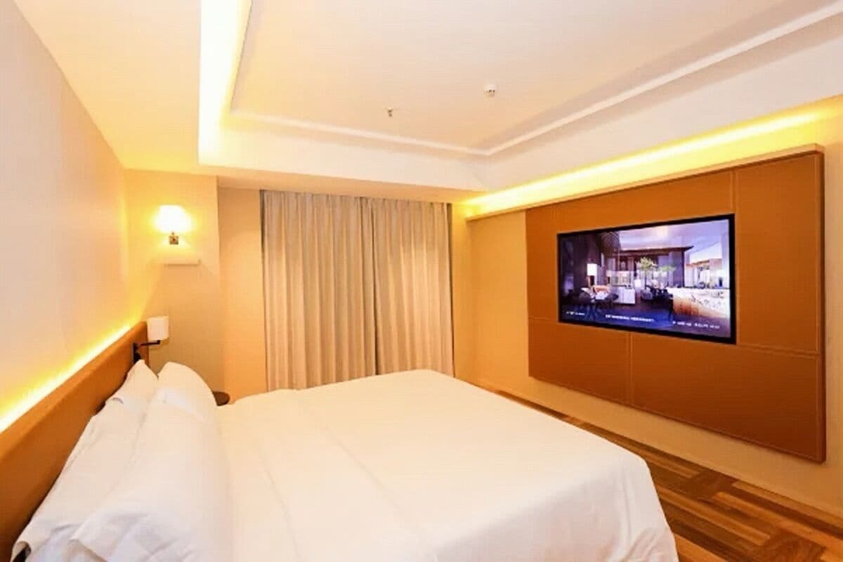 A hotel room with a bed, a television mounted on the wall, and a curtain.