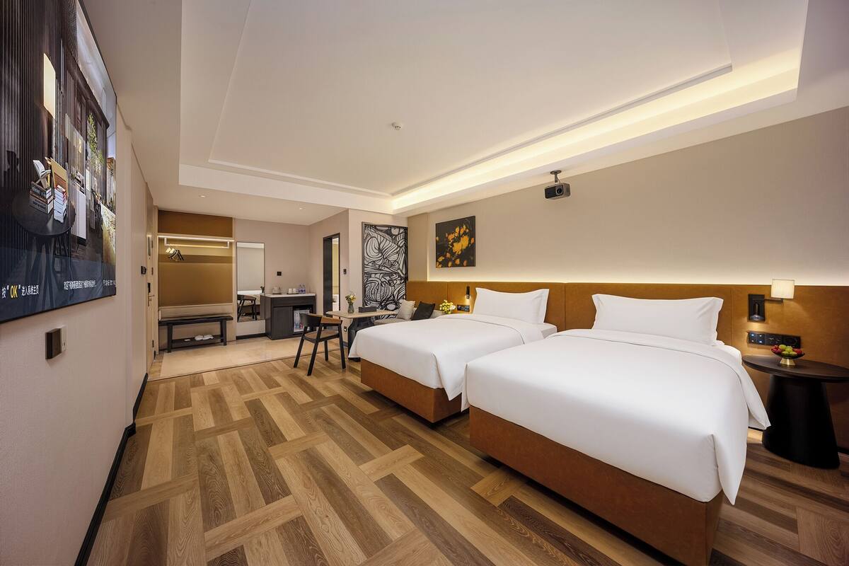 Ein Hotelzimmer mit zwei Betten, einem Schreibtisch, einem Stuhl, einem Spiegel und Bildern an den Wänden.