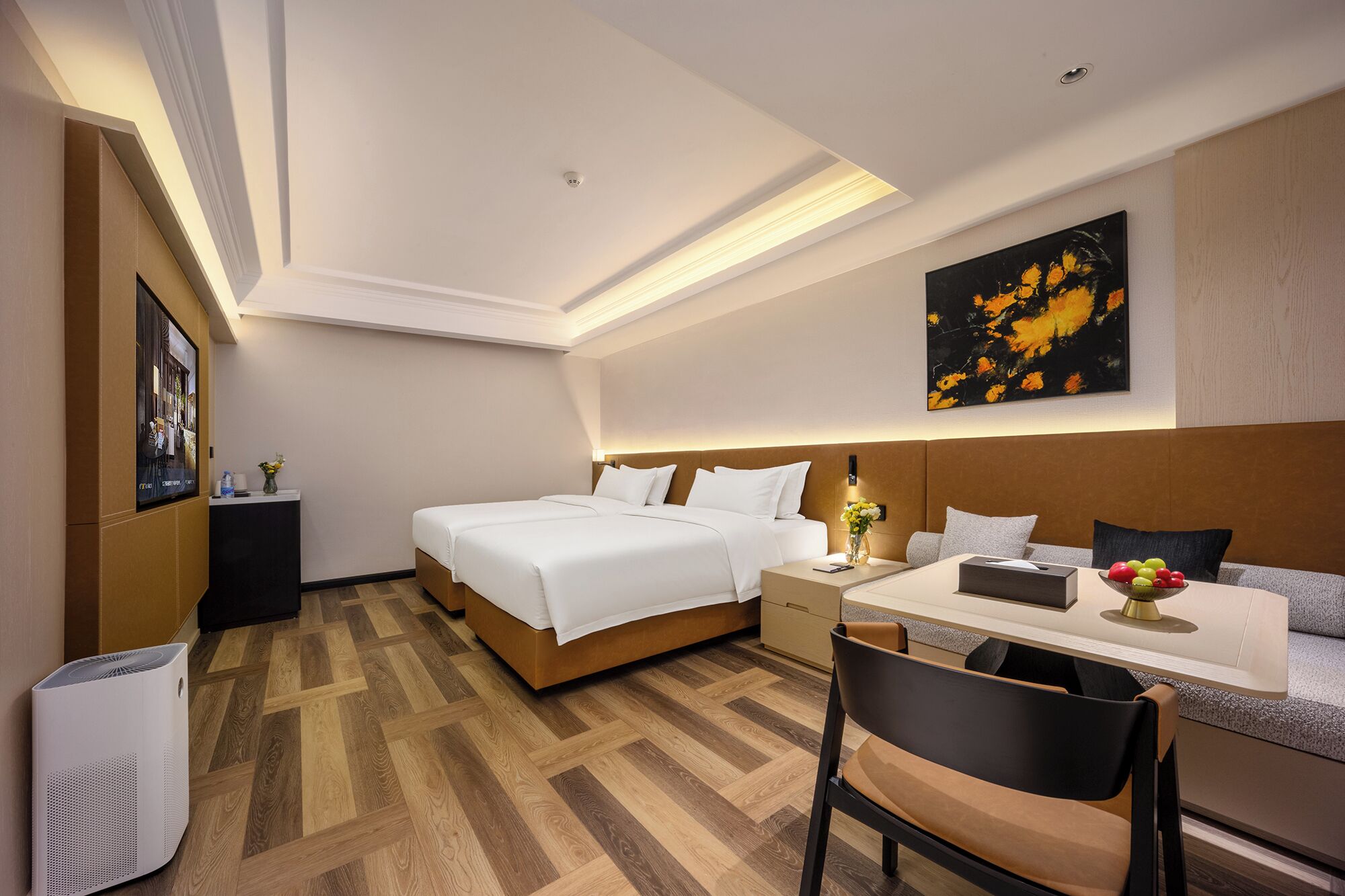 Habitación de hotel con cama doble, escritorio con silla, mesita de noche, televisor montado en la pared y una pintura.