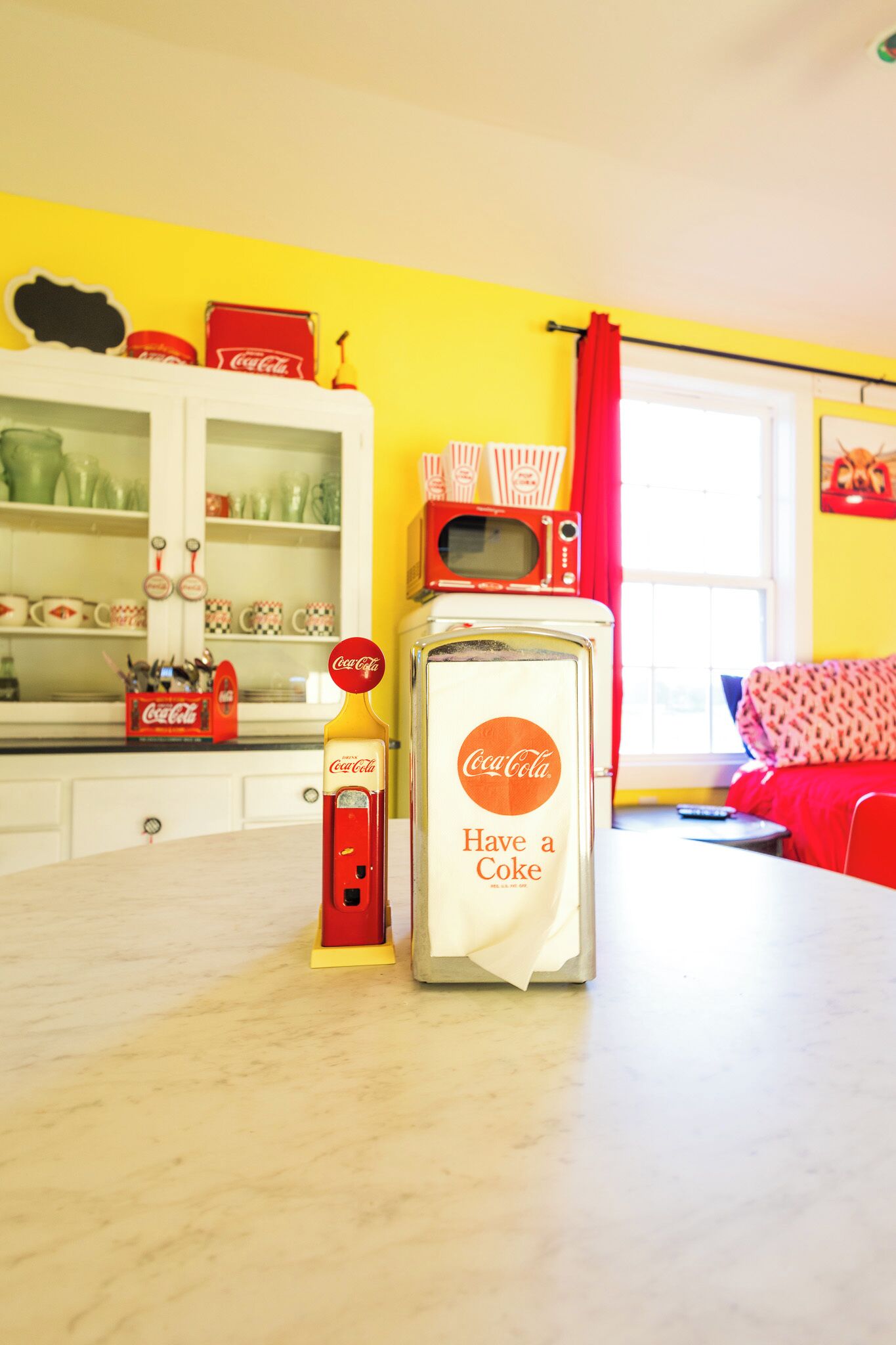 A kitchen with a vintage refrigerator, a microwave, and a Coca-Cola dispenser.