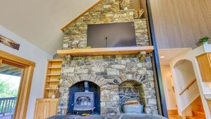 A stone fireplace with a TV above it, wooden shelves, and a staircase.