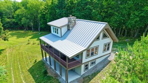 A two-story house with a balcony, a stone chimney, and a surrounding wooded area.