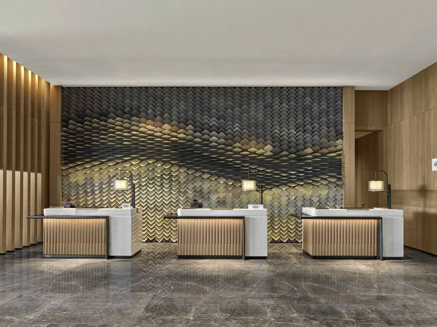A hotel reception area with three counters, a patterned wall, and a marble floor.