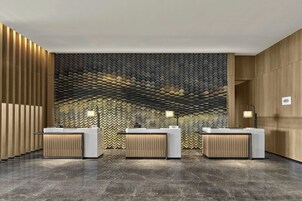 Et hotelreceptionsområde med tre skranker, en mønstret væg og en marmorgulv.