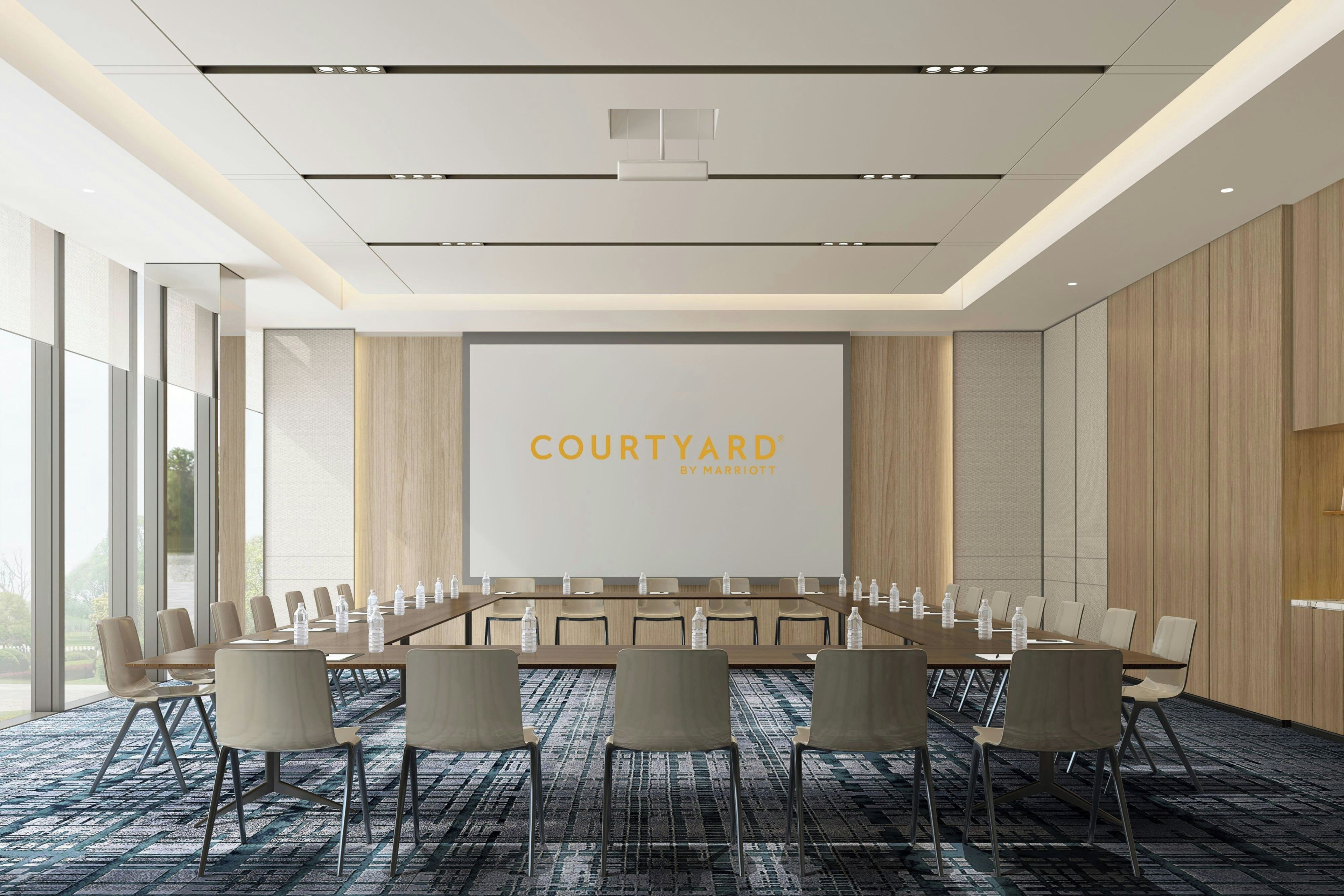 Un salón de conferencias con una larga mesa, sillas y una pantalla grande que muestra 'COURTYARD BY MARRIOTT'.