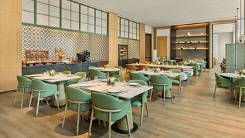 A restaurant with multiple tables and chairs, a counter with a coffee machine, and shelves with decorative items.
