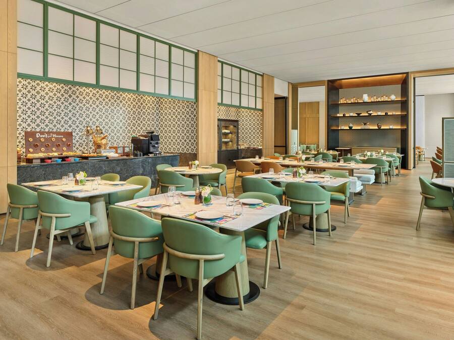 A restaurant with multiple tables and chairs, a counter with a coffee machine, and shelves with decorative items.