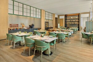 Un restaurante con varias mesas y sillas, una barra con una máquina de café y estantes con objetos decorativos.