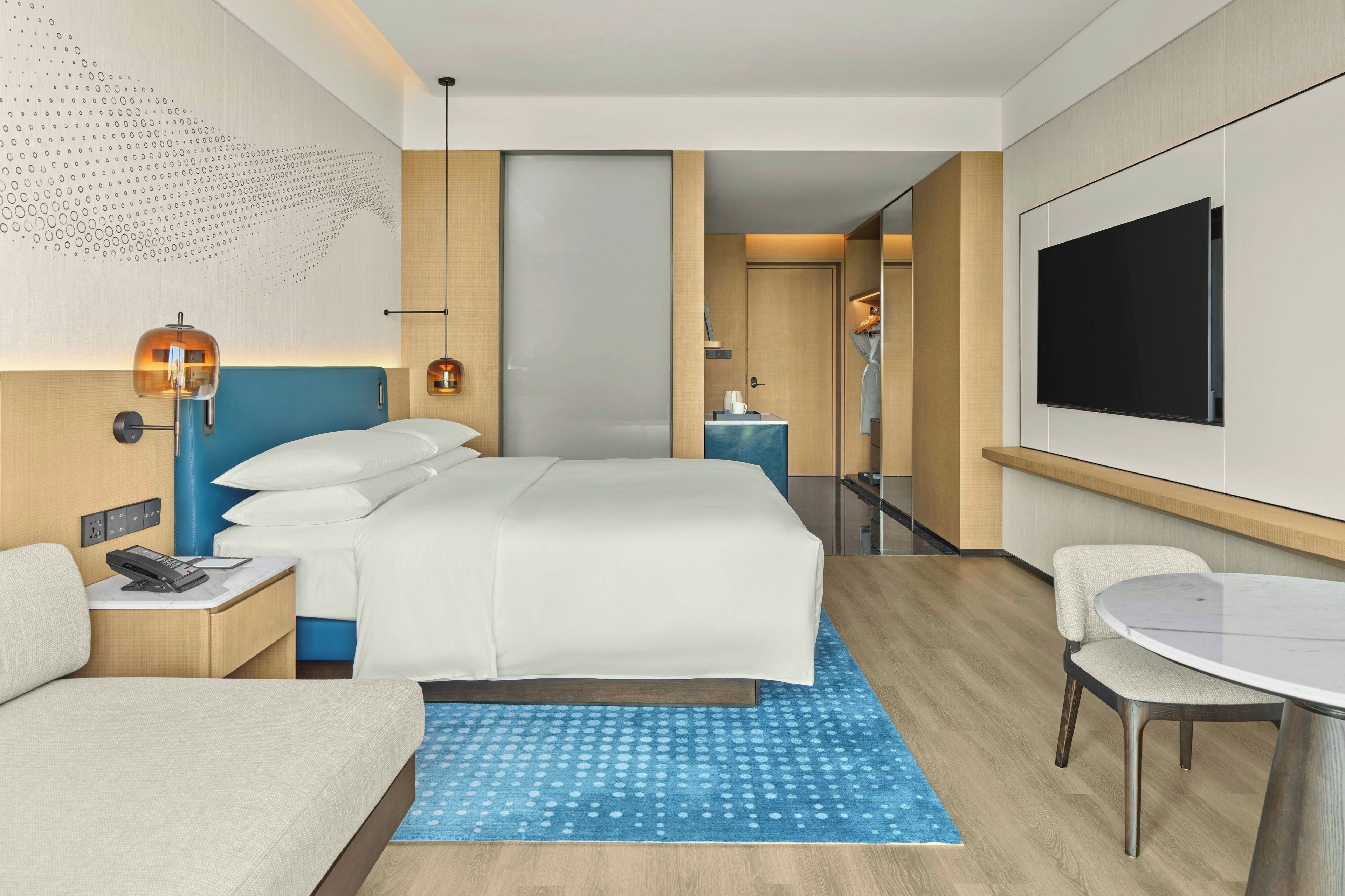 Ein Hotelzimmer mit Bett, Schreibtisch, Stuhl, Fernseher und einem gemusterten Teppich.