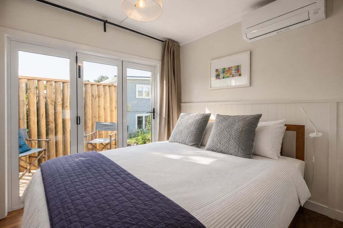 A bedroom with a bed, a window, an air conditioning unit, and a view of the outside.