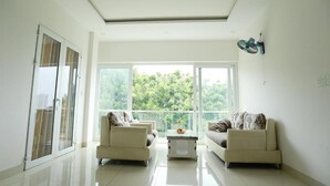 A modern living room with two sofas, a coffee table, and large windows offering a view of greenery.