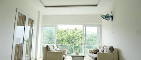 A modern living room with two sofas, a coffee table, and large windows offering a view of greenery.