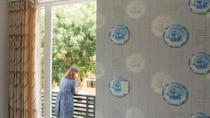 A room with patterned wallpaper, a window with curtains, and a view of a balcony.