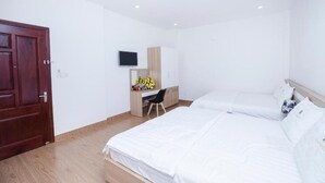 A hotel room with a wooden door, a desk with a chair, a bed, and a TV mounted on the wall.