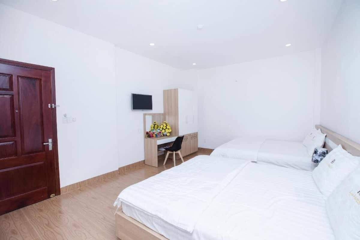 A hotel room with a wooden door, a desk with a chair, a bed, and a TV mounted on the wall.