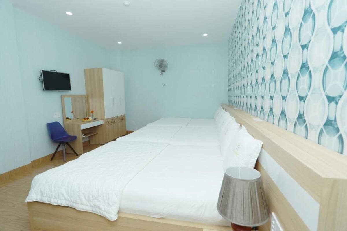 A bedroom with two beds, a desk, a chair, a TV, a fan, and a patterned wall.
