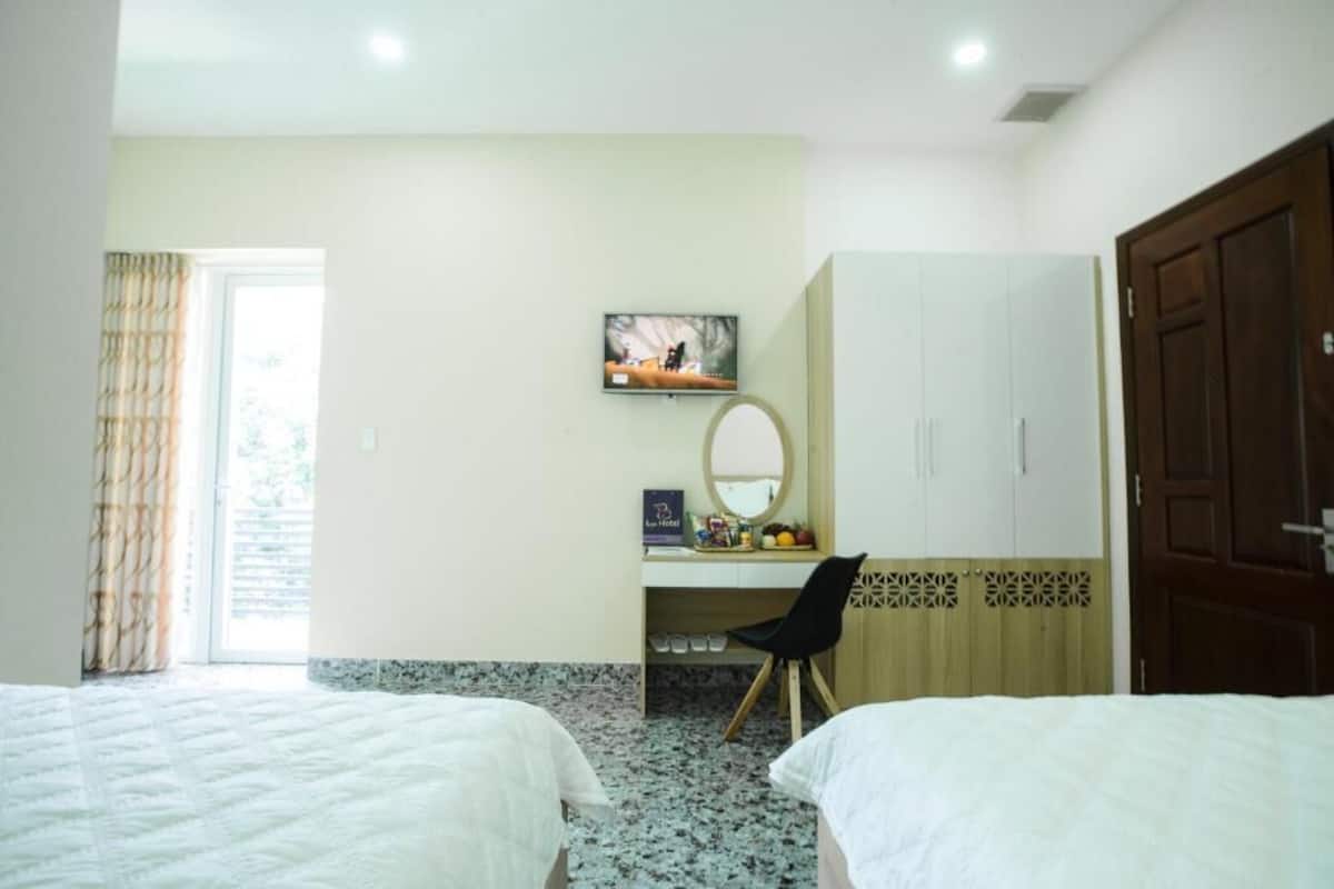 A hotel room with two beds, a desk with a mirror, a TV, and a wardrobe.