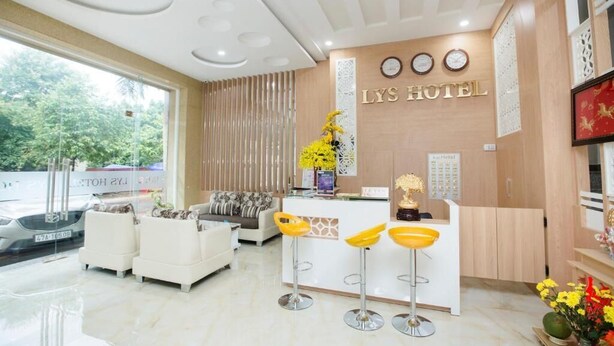 A modern hotel reception area with a white reception desk, three yellow bar stools, a sofa, and a decorative vase with yellow flowers.