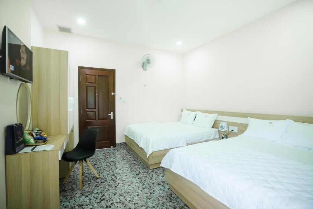 Una habitación de hotel con dos camas, un escritorio con silla, un televisor y una puerta.